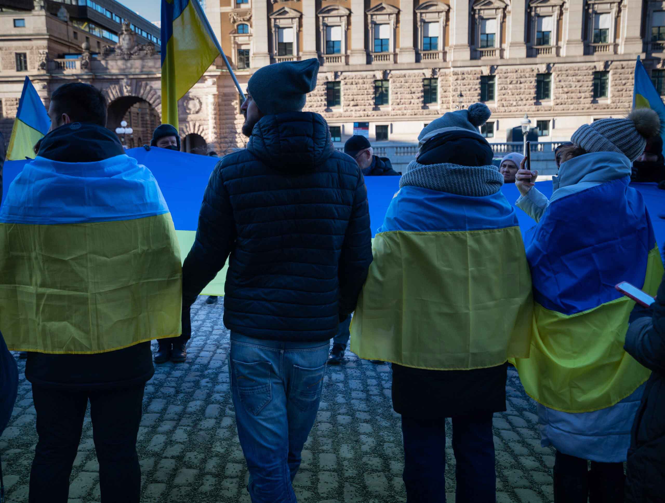 Many people hold hands in solidarity with ukrainian flags on their back